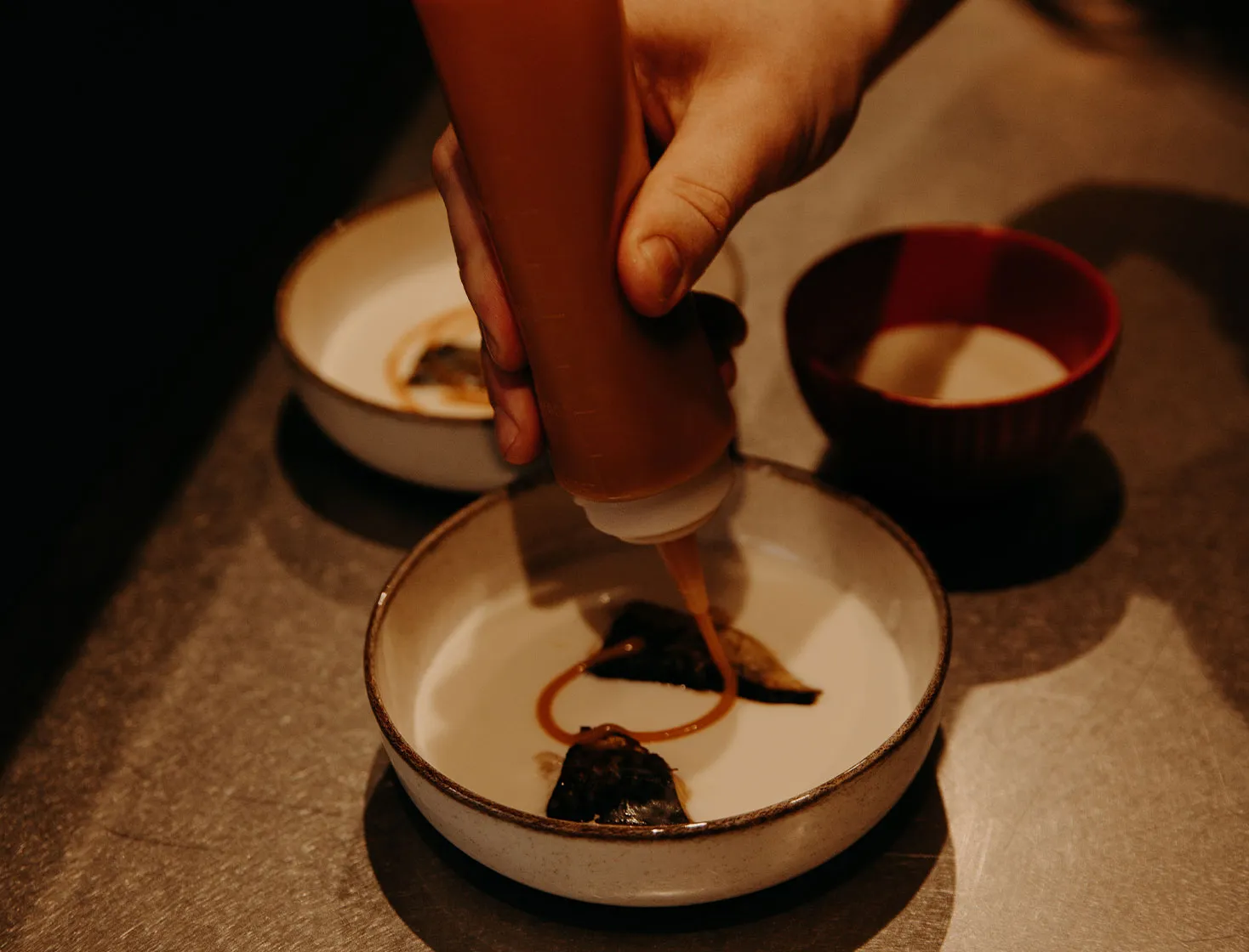 Au coeur des cuisines Nathanaël Fromont avec l'ajout d'une sauce pour parfaire un délicieux plat.